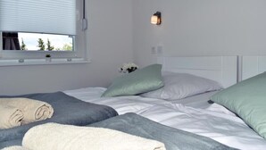 Un dormitorio con cama, almohadas, una ventana con persianas y una lámpara fijada a la pared.