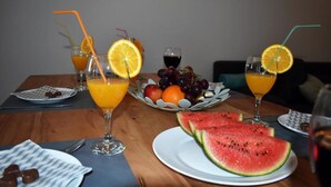 Una mesa de comedor con dos vasos de zumo de naranja, un plato de sandía en rodajas y una cesta de frutas variadas.