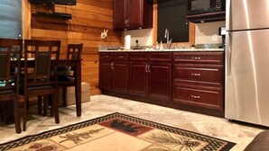 Una cocina con armarios de madera, un refrigerador de acero inoxidable, un microondas y una zona de comedor con sillas y una mesa.