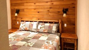 Un dormitorio con paneles de madera, una cama, dos mesitas de noche y lámparas fijadas a la pared.