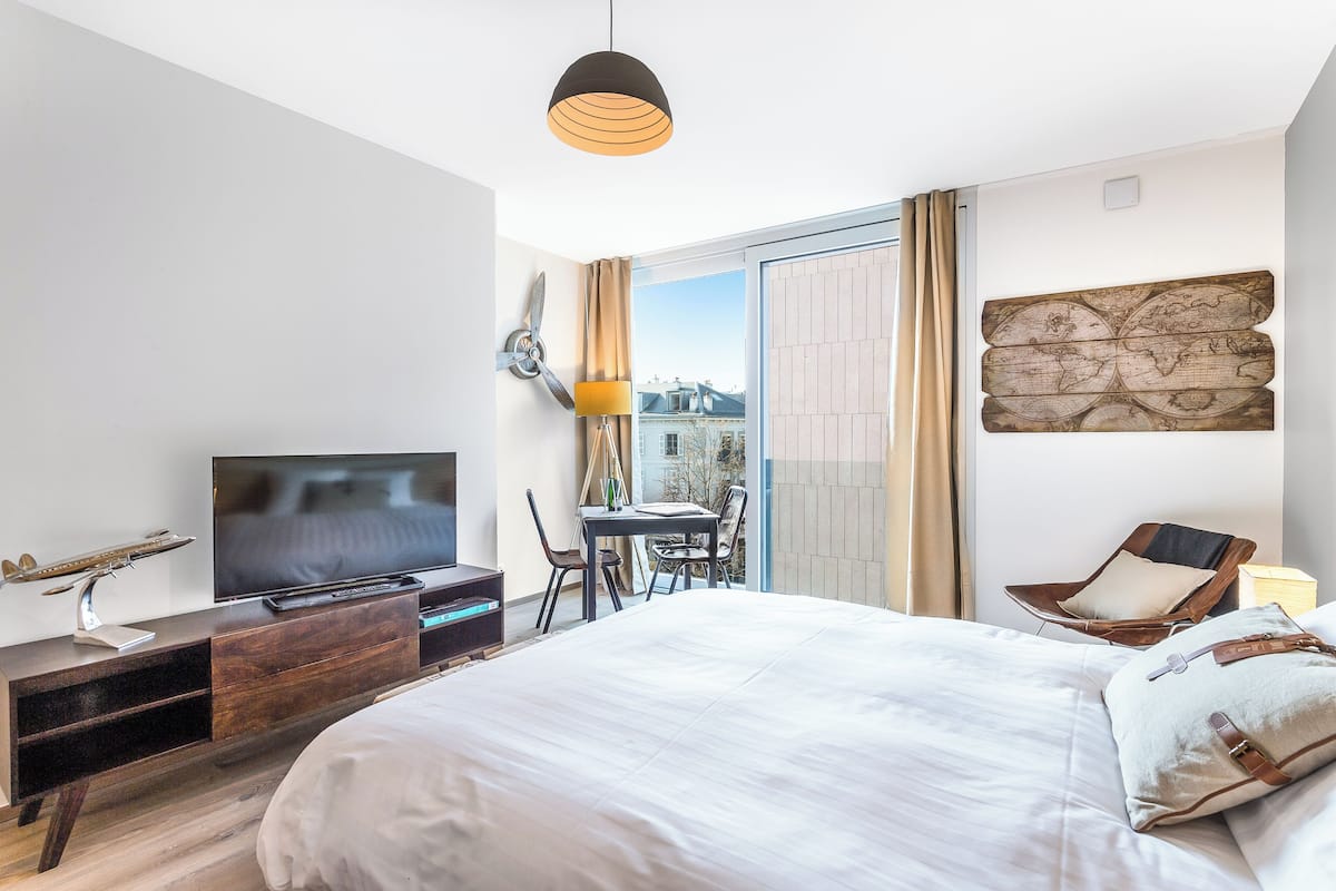 A modern hotel room with a large bed, a flat-screen TV, a wooden desk, and a chair.