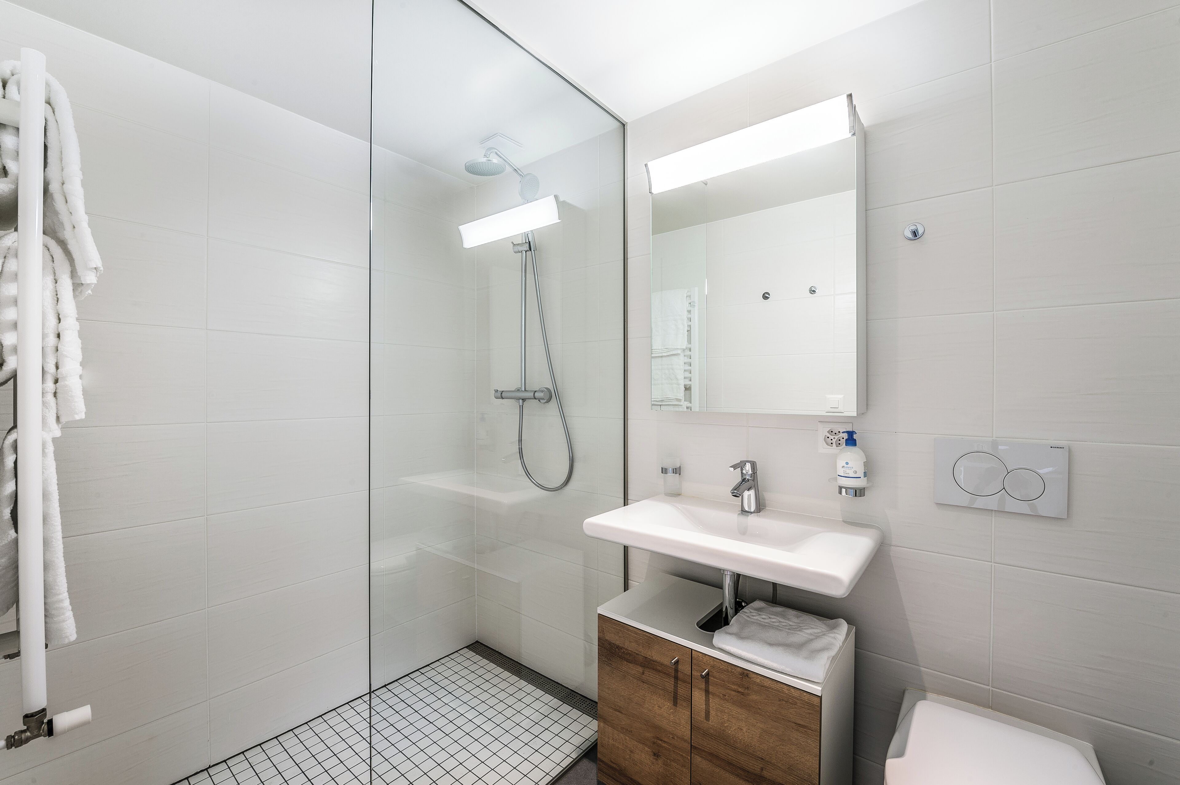 A modern bathroom with a glass-enclosed shower, a white sink, a wooden cabinet, and a mirror.