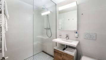 A modern bathroom with a glass-enclosed shower, a white sink, a wooden cabinet, and a mirror.