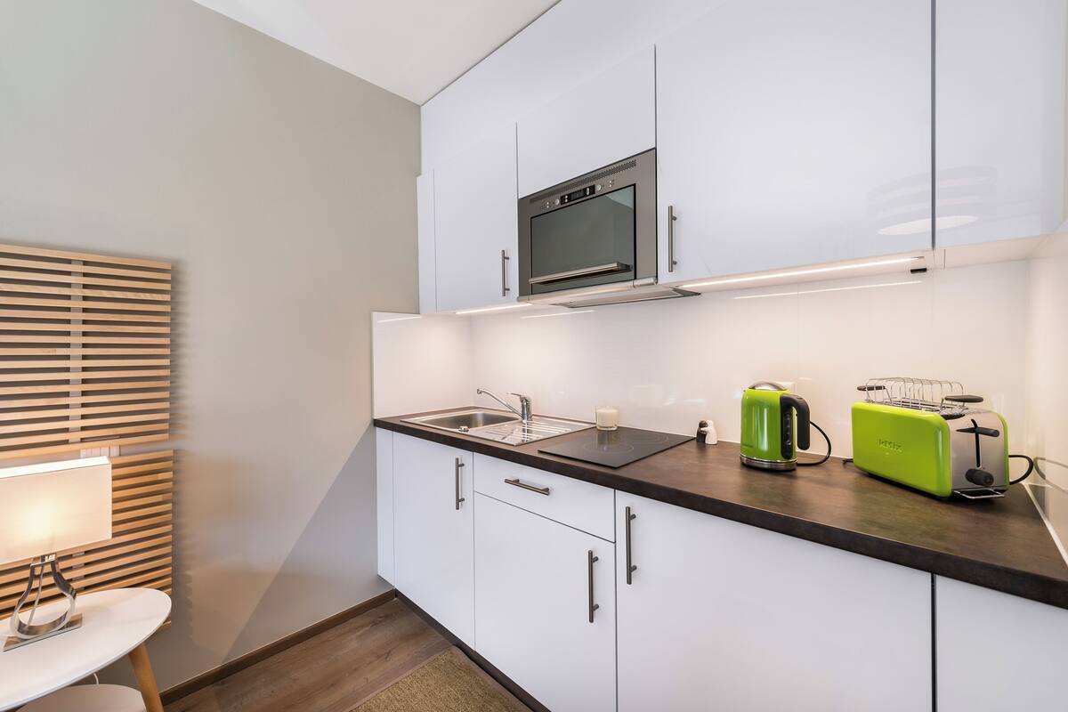 A modern kitchen with white cabinets, a built-in oven, a sink, a kettle, and a toaster.