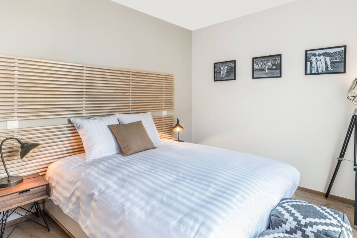 A bedroom with a large bed, wooden blinds, a bedside lamp, a floor lamp, and three framed pictures on the wall.