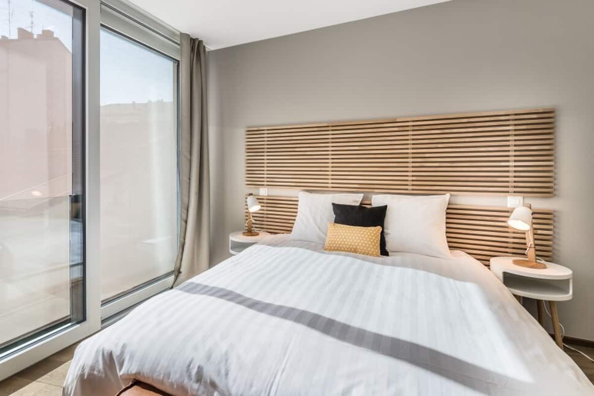 A modern hotel room with a large bed, wooden headboard, and a view through a large window.