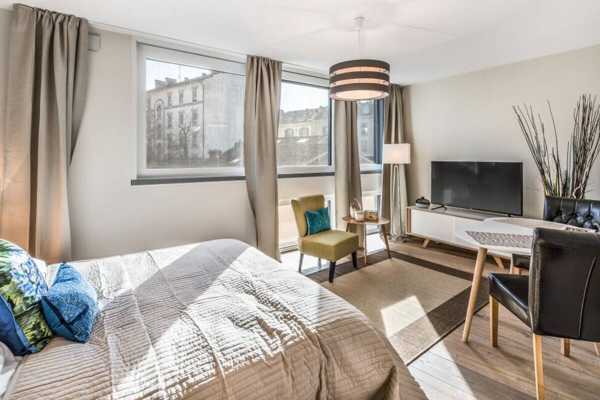 A hotel room with a bed, a desk, a chair, a TV, and a window with a view of buildings.
