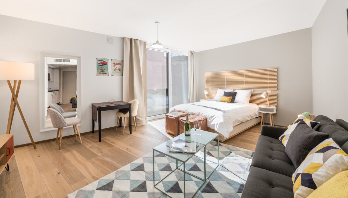 A modern hotel room with a bed, a desk, a sofa, and a glass coffee table.