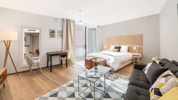 A modern hotel room with a bed, a desk, a sofa, and a glass coffee table.
