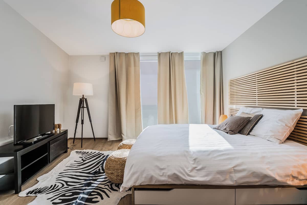 A modern bedroom with a bed, a TV, a lamp, and a view of the outdoors.