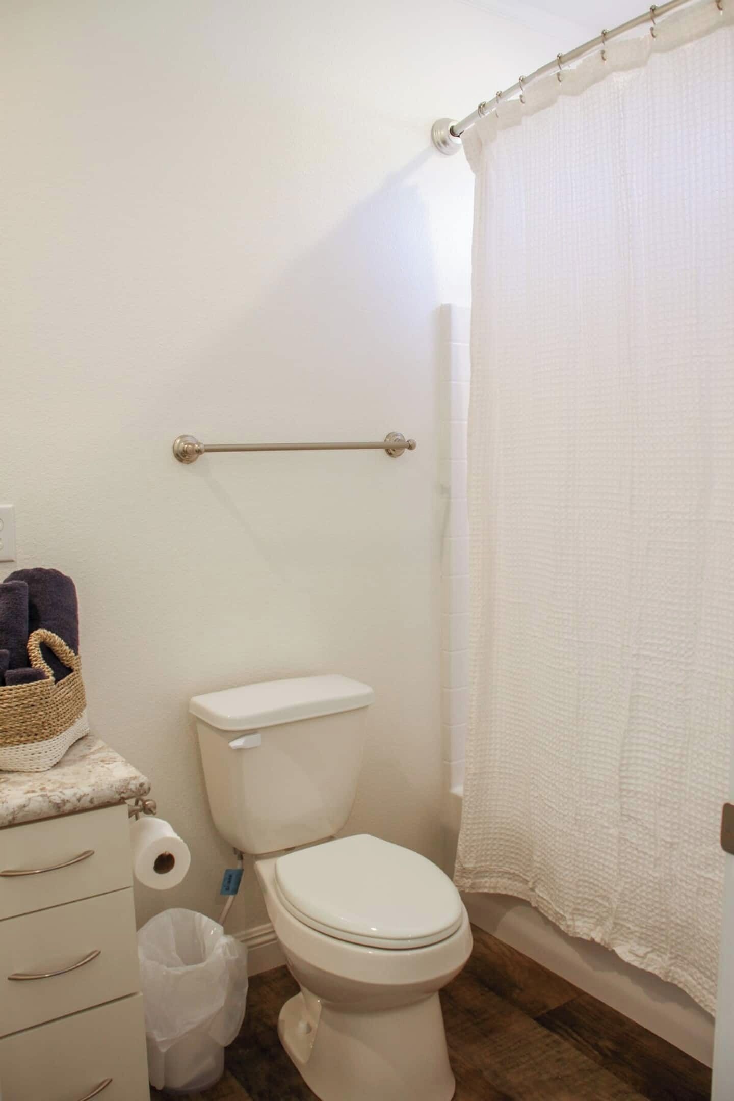 A bathroom with a toilet, a towel rack, a basket, and a shower curtain.