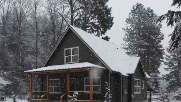 A two-story cabin with a covered porch and snow-covered surroundings.