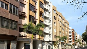 Un edificio residencial de varios pisos con balcones, un local comercial en la planta baja y palmeras.