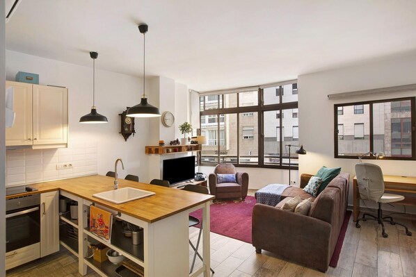 A modern apartment with a kitchen, dining area, and living room. It features large windows, a fireplace, and a cozy seating area.