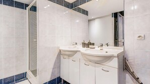 Un baño moderno con dos lavamanos, una ducha y un espejo grande.