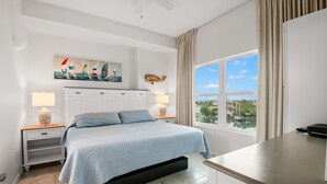 A bedroom with a bed, two bedside tables with lamps, a window with a view, and a painting on the wall.