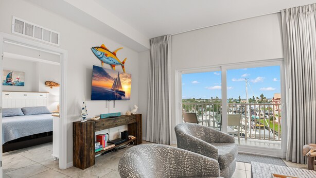A living room with a bed, a TV, a large window with a view of the city, and a balcony.