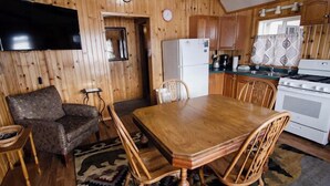 A wooden interior with a dining table, chairs, a sofa, a TV, a refrigerator, and a stove.