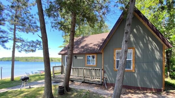 A cabin with a deck, a grill, and a view of a lake.