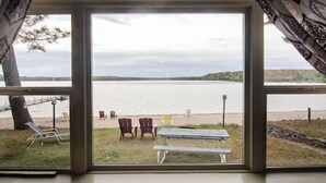 A view through a window of a lakeside area with a bench, chairs, and a picnic table.
