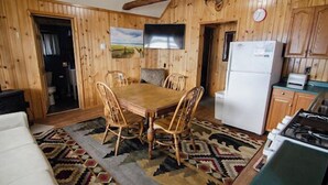 A wooden interior with a dining table, chairs, a refrigerator, and a kitchen area.