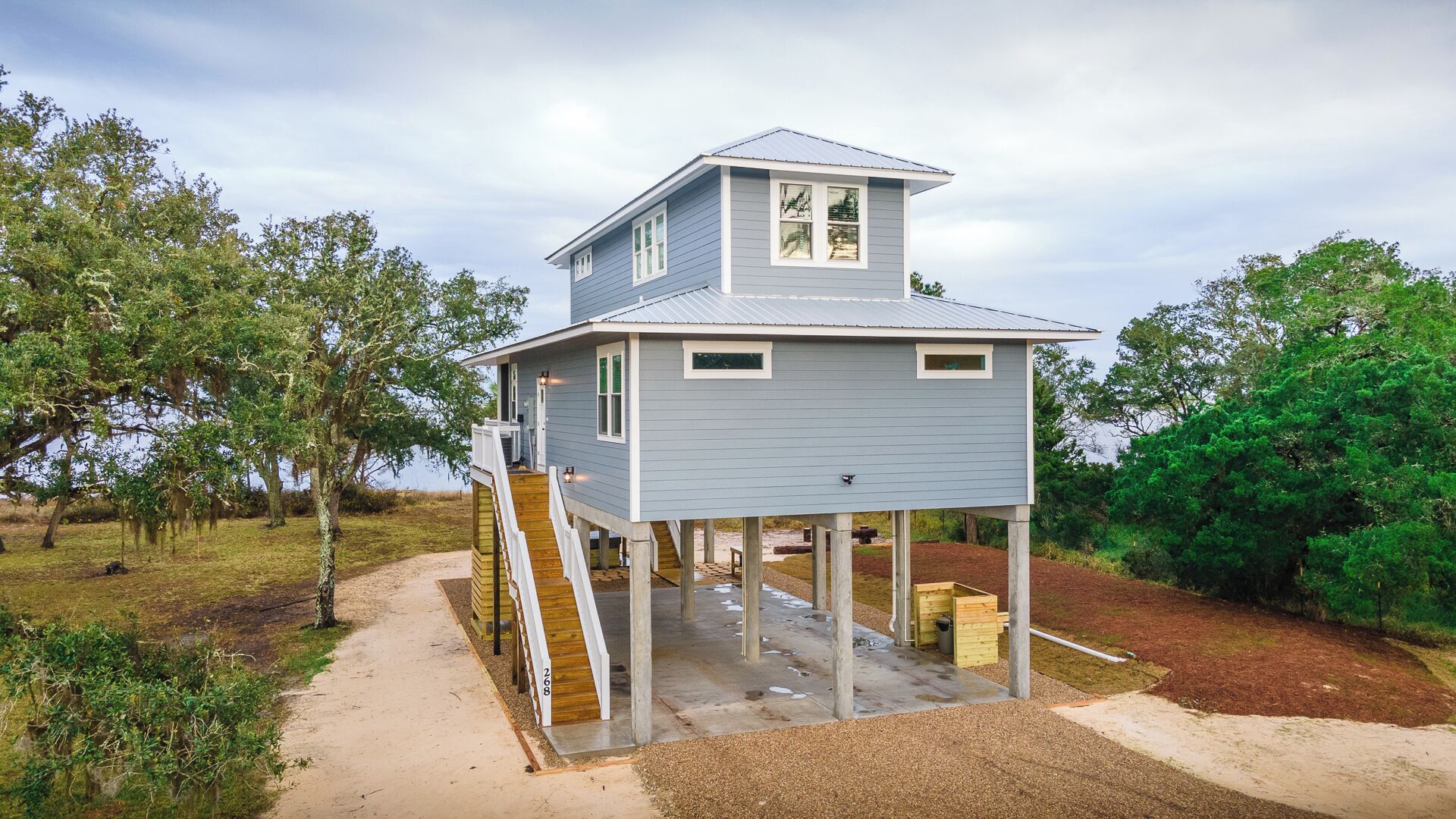 Une maison à deux étages avec une terrasse, entourée d’arbres et sous un ciel dégagé.