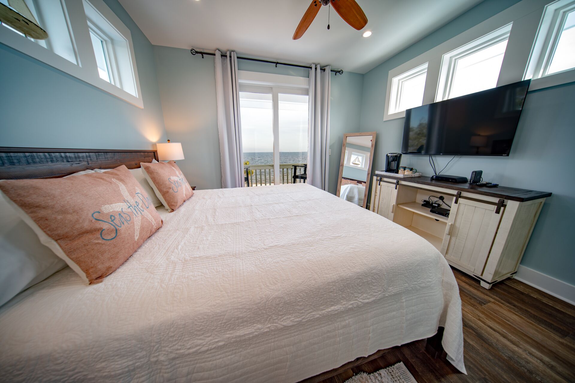 A bedroom with a large bed, a ceiling fan, a TV, and a view of the sea.