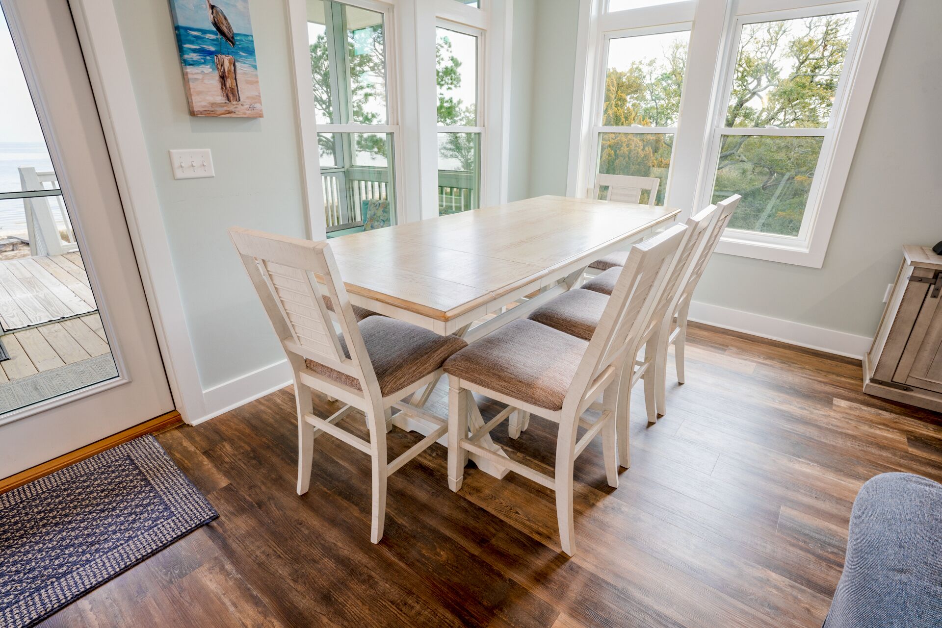 Een eetgedeelte met een houten tafel en vier stoelen, grote ramen en uitzicht op de omgeving.