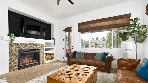 A living room with a fireplace, a television mounted on the wall, a brown leather sofa, and a wooden coffee table. - Mountain View with Hot Tub/AC nestled in the pines  (Flagstaff)