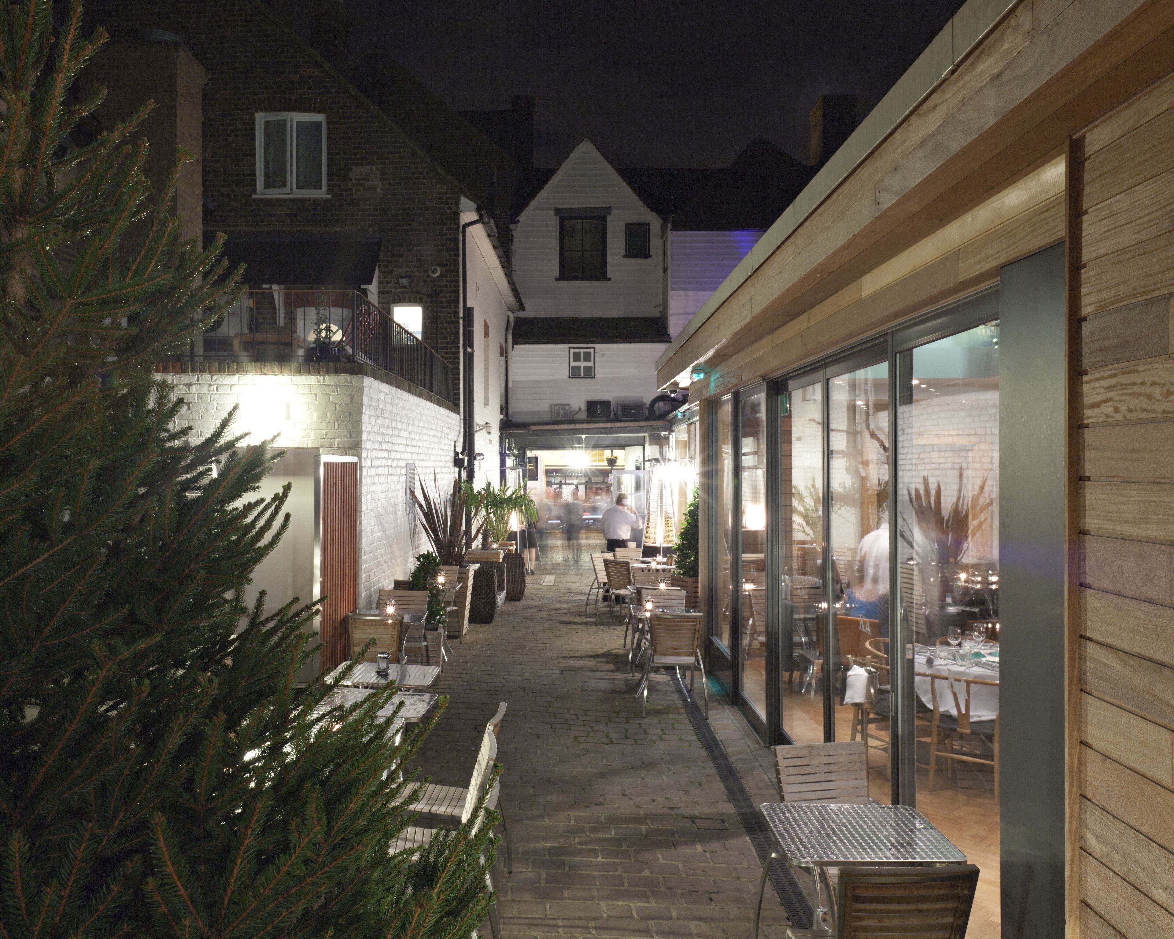 An outdoor cafe area with tables and chairs, a Christmas tree, and a building with large windows.