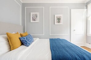 A bedroom with a bed, two pillows, a blue blanket, and two framed pictures on the wall.
