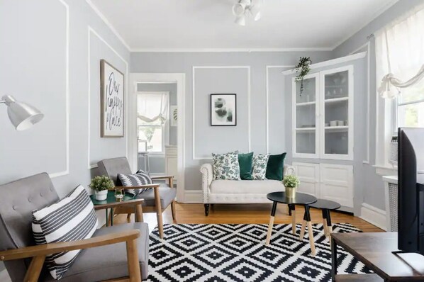 A living room with a grey sofa, a striped armchair, a patterned rug, and a white cabinet with glass doors.