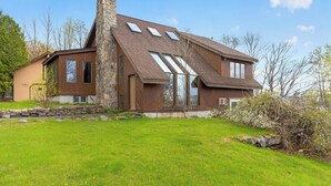 A modern house with a stone chimney, large windows, and a well-maintained lawn.