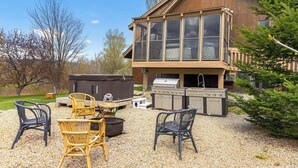 A wooden cabin with a deck, outdoor seating, and a grill area.