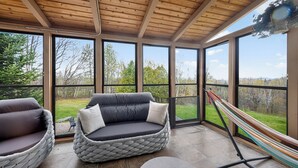 A sunroom with a cushioned seating area, large windows, and a hammock.