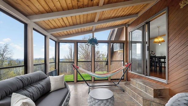 A covered outdoor seating area with a hammock, a cushioned sofa, and a round table.