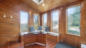 A wooden cabin interior with a glass-top table, large windows, and a tiled floor.