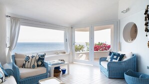 Ein helles, luftiges Wohnzimmer mit Meerblick, ausgestattet mit Rattanmöbeln und einem weißen Fliesenboden.
