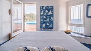Ein Schlafzimmer mit Bett, Meerblick, einer Tür zu einem Balkon und Wandbildern von Segelbooten.