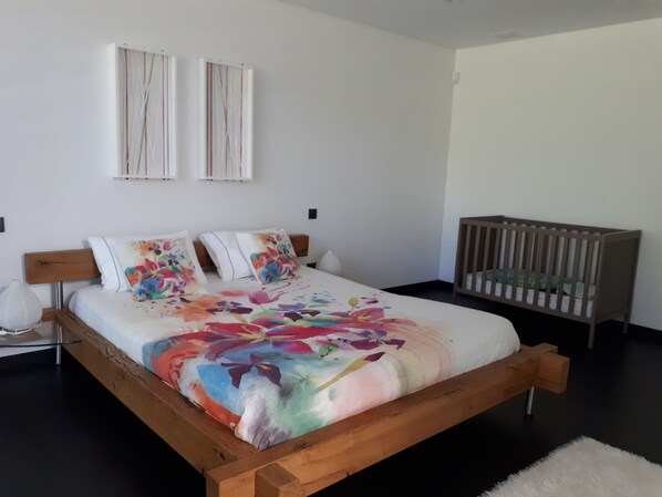 Un dormitorio con una cama de madera, una cuna y dos lámparas fijadas a la pared.