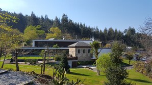 A modern house with a stone facade, surrounded by a well-maintained garden and a forested hillside.