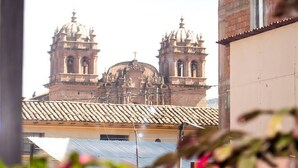 Vista de una iglesia histórica con dos torres de campanas y una cúpula central, visible a través de una ventana con vistas a un edificio y algo de vegetación en primer plano.