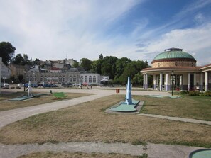 Ein Park mit einem Kiosk, einer Fontäne und einem Gebäude mit Kuppel im Hintergrund.