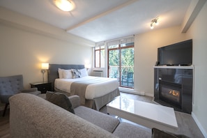 Ein Hotelzimmer mit Bett, Sofa, Fernseher, Kamin und einem Balkon mit Aussicht.