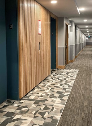 Ein Hotelkorridor mit Holzwandverkleidung, einem gemusterten Teppich und nummerierten Türen, einschließlich Tür Nummer 3.