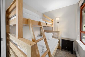 Ein Stockbett mit Holtzargen und weißer Bettwäsche, ein Nachttisch und eine Lampe.