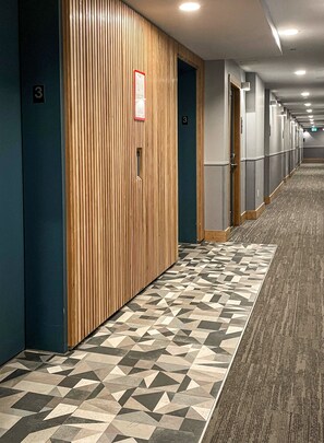 Corredor de hotel com lambris de madeira, carpete estampado e portas numeradas 3.