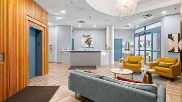 A modern lobby with a reception desk, a grey sofa, yellow armchairs, and a wooden wall.