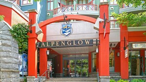 Een gebouw met een opvallend 'ALPENGLOW'-bord, stenen treden die naar de ingang leiden en een balkon met een hekwerk.