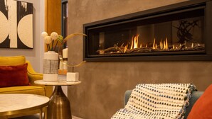 Een moderne woonkamer met een open haard, een gele bank, een ronde salontafel en een decoratieve vaas.